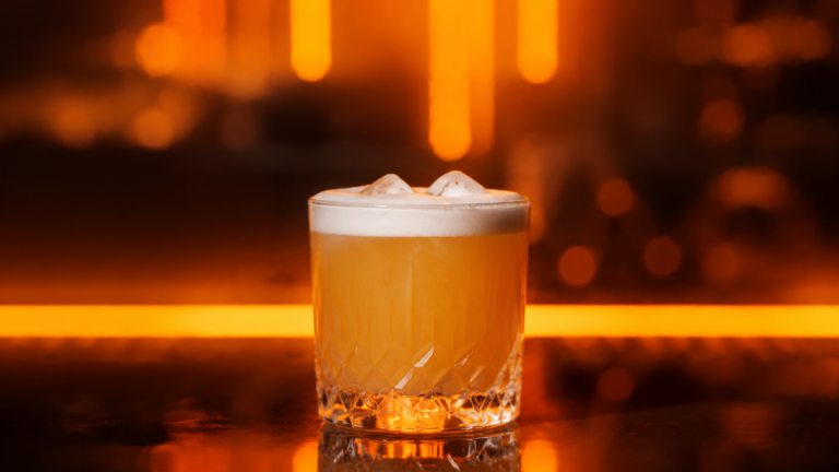 Amaretto Sour vor extrem unscharfem Neonhintergrund in der Farbe des Drinks